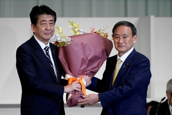 지난해 9월 14일 일본 도쿄의 자민당 본부에서 아베 신조 당시 일본 총리(왼쪽)가 스가 요시히데 당시 관방장관에게 자민당 총재 선거 축하 꽃다발을 건네고 있다.로이터뉴스1