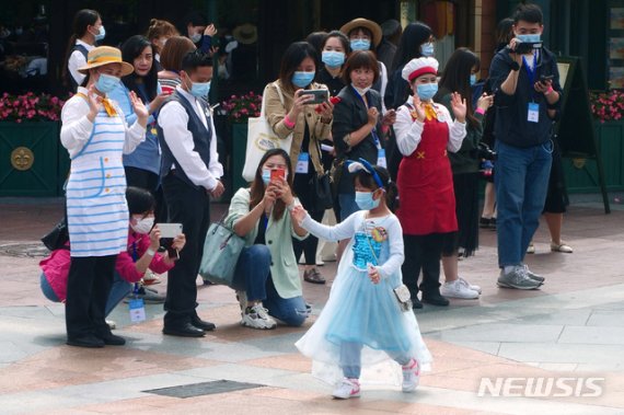 [상하이=AP/뉴시스]11일(현지시간) 중국 상하이 디즈니랜드 테마파크가 재개장한 가운데 마스크를 쓴 한 소녀가 직원들의 환영을 받으며 입장하고 있다. 2020.05.11.