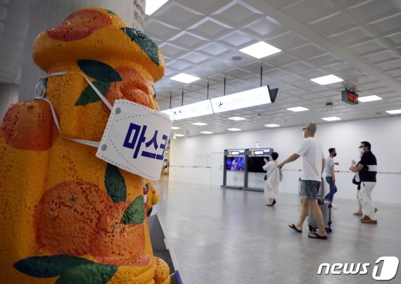 제주국제공항에서 마스크를 쓴 돌하르방 앞으로 관광객들이 지나가고 있다. 2020.8.30 /뉴스1 © News1 홍수영 기자