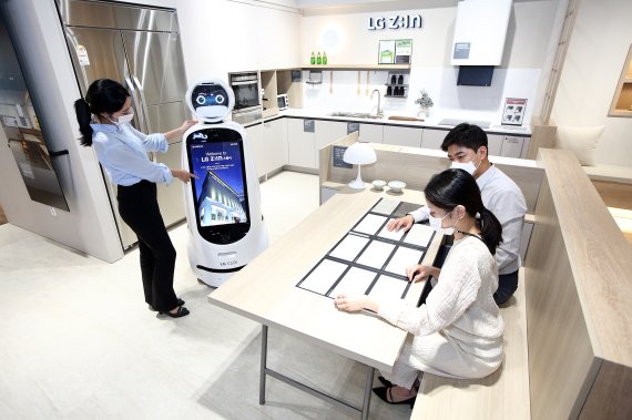 LG하우시스가 서울 논현동 가구거리에 위치한 플래그십 전시장 'LG Z:IN 스퀘어'에 LG전자의 자율주행 안내로봇 'LG 클로이 안내로봇'을 도입, 방문 고객이 직원 도움 없이도 전시장을 둘러볼 수 있는 비대면 서비스를 확대하고 있다. LG지인 스퀘어를 방문한 고객들이 'LG 클로이 안내로봇'의 설명을 들으며 주방공간을 살펴보고 있다.