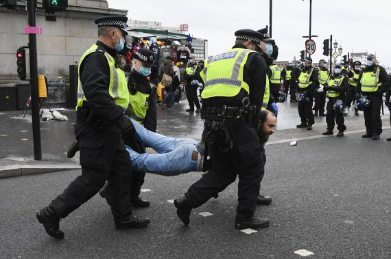 영국 경찰이 24일(현지시간) 런던 웨스트민스터 브리지에서 코로나19 방역조처에 항의하는 시위자 1명을 들고 가고 있다. 사진=AP뉴시스