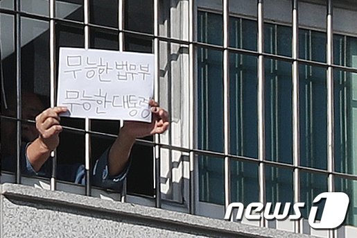 지난 6일 오후 서울 송파구 동부구치소에서 한 재소자가 '무능한 법무부, 무능한 대통령'이라는 문구가 적힌 종이를 창살 너머로 꺼내 보이고 있다. 뉴스1
