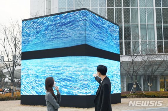 [서울=뉴시스] LG전자가 서울 송파구 롯데백화점 에비뉴엘 월드타워점 6층 아트홀에서 열리고 있는 고(故) 김환기 화백 작품 미디어 전시에 LED 사이니지, 올레드 TV 등을 설치했다. 모델들이 전시장 외부 롯데월드타워 야외 공간에 실외용 LED 사이니지를 이어 붙여 만든 가로, 세로, 높이 각 6미터 크기의 미디어큐브를 통해 작품을 감상하고 있다. (제공=LG전자)