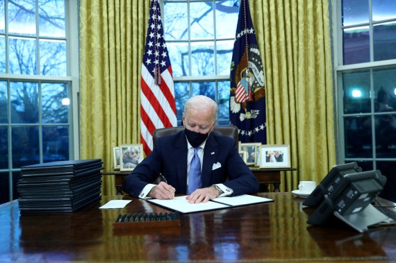 조 바이든 신임 미국 대통령이 20일(현지시간) 미국의 제46대 대통령으로 취임한 후 백악관 대통령 집무실에 앉아, 서류를 펼쳐놓고 서명을 하고 있다. 로이터 뉴스1
