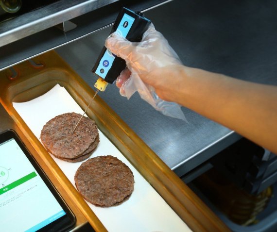 맥도날드 매장 직원이 디지털 온도계를 사용하여 조리 후 패티의 중심 온도를 측정하고 있다. 측정 온도는 태블릿에 자동 전송되어 기록, 관리된다.