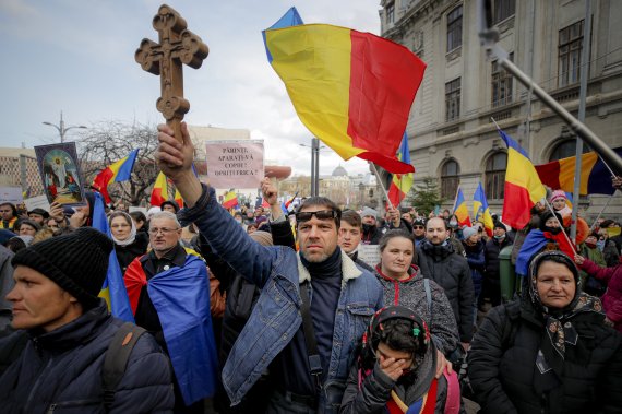 20일(현지시간) 루마니아 수도 부쿠레슈티에서 코로나19 백신 반대 집회가 열려 시위대가 루마니아 국기를 흔드는 가운데 한 남성이 나무 십자가를 들고 있다. 코로나19 감염이 급증하는 와중에 수백 명의 백신 반대 시위대가 거리로 나왔다. 뉴시스화상