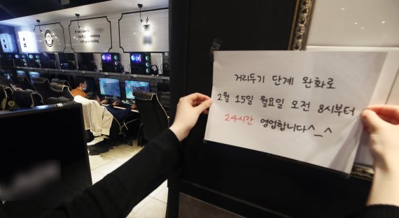 [서울=뉴시스]김병문 기자 = 사회적 거리두기가 2단계로 완화되며 다중이용시설에 대한 영업시간 제한 해제를 하루 앞둔 14일 오후 서울 시내 한 PC방에서 직원이 24시간 영업을 알리는 안내문을 부착하고 있다. 2021.02.14. dadazon@newsis.com