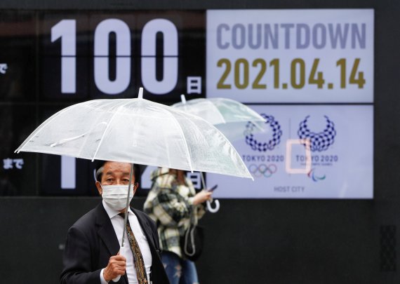 도쿄올림픽 개막까지 100일을 남겨둔 지난 14일 도쿄에 비가 내렸다. 한 남성이 우산을 쓰고, 도쿄올림픽 로고 앞을 지나고 있다. 로이터 뉴스1