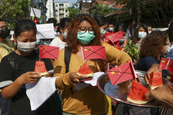 [양곤=AP/뉴시스]13일 미얀마 양곤에서 반 쿠데타 시위대가 훼손한 중국 국기를 수박 조각에 꽂아 들고 있다. 시위대는 미얀마 시장 내 일부 국내 상품의 가격에 영향을 끼친 중국과의 교역을 중단할 것을 촉구하고 있다. 2021.04.13.