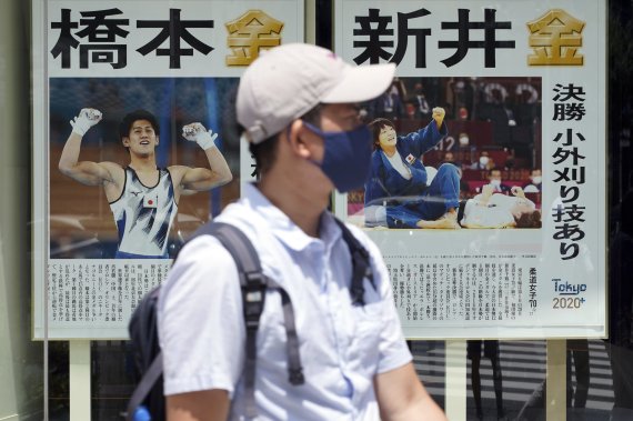 마스크를 한 남성이 29일 일본 도쿄의 한 거리에 부착된 도쿄올림픽 남자 체조경기에 출전한 하시모토 다이키 선수의 금메달 소식을 전하는 신문 기사 앞을 지나가고 있다. AP뉴시스