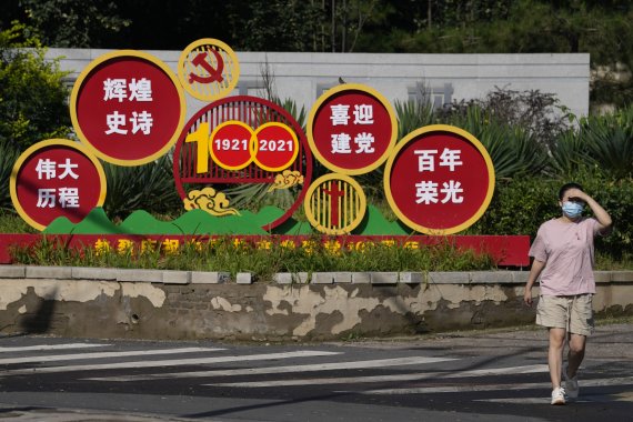A woman walks past propaganda promoting the centennial of the founding of the Chinese Communist Party in Beijing on Aug. 24, 2021. An avalanche of changes launched by China's ruling Communist Party has jolted everyone from tech billionaires to school kids. Behind them: President Xi Jinping's vision 