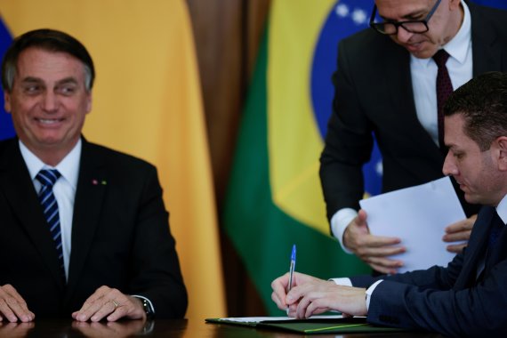 19일(현지시간) 브라질 브라질리아의 대통령궁에서 자이르 보우소나루 브라질 대통령(왼쪽)이 콜롬비아 정상과 회동 가운데 연방경찰 관계자의 서명 모습을 보고 있다.로이터뉴스1