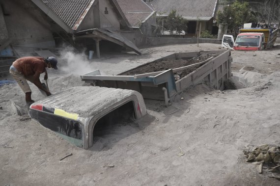 5일 인도네시아 자바섬 동부지역에서 한 남성이 화산재에 묻힌 차량 옆에서 복구 작업을 하고 있다. AP뉴시스