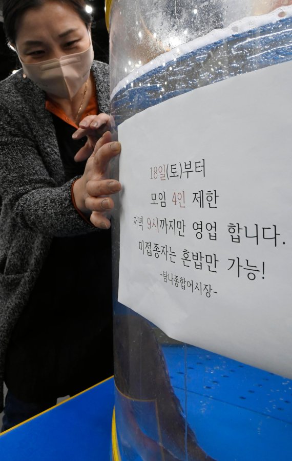 16일 경기 의왕시 한 횟집 사장이 18일부터 적용되는 거리두기 조정방안 안내문을 붙이고 있다. 이날 정부 거리두기 조정방안에 따르면 전국 사적모임 인원은 4인, 식당·카페 등 운영시간은 오후 9시까지로 제한된다. 사진=박범준 기자