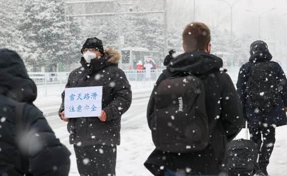 2022 베이징 동계올림픽 개막 후 첫 눈이 내리는 13일 중국 베이징 메인미디어센터 앞 버스 하차장에서 한 관계자가 '눈길 조심하세요'라는 표지를 들고 있다. 2022.2.13/뉴스1 © News1 안은나 기자
