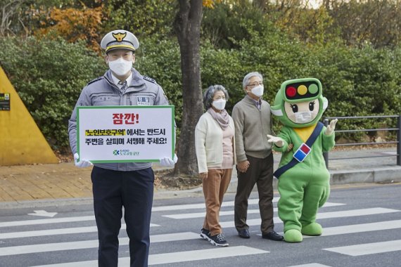 노인보행자를 배려하자는 경찰관의 안내판 뒤에서 노인들이 도로교통공단 마스코트 호순이의 안내를 받으며 횡단보도를 건너고 있다. (도로교통공단 제공) 2020.11.27/뉴스1 © News1 전민기 기자