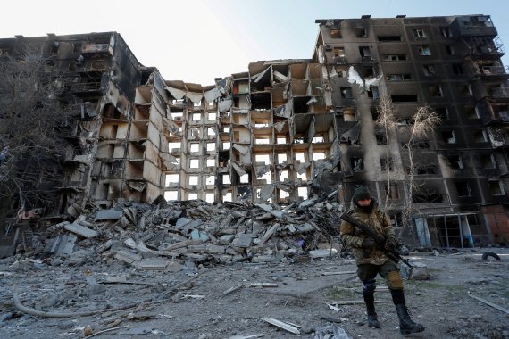 친러시아군 병사가 3월28일(현지시간) 우크라이나 남부도시 마리우폴의 한 파괴된 아파트 앞을 걷고 있다. 2022.03.28/뉴스1 © 로이터=뉴스1 © News1 김민수 기자