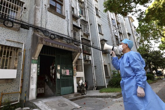 코로나19 봉쇄령이 내려진 중국 상하이에서 방역복을 입은 봉사자가 지난 12일 마이크를 통해 아파트 주민들에게 유의사항을 전달하고 있다. AP신화통신