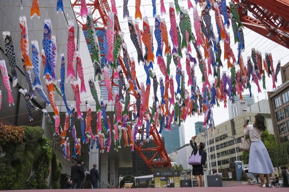 [도쿄=AP/뉴시스] 27일 일본 도쿄에서 시민들이 도쿄 타워에 설치된 화려한 잉어 깃발 '고이노보리'의 사진을 찍고 있다. 고이노보리는 남자아이의 성장과 출세를 기원하는 전통 관습으로 5월 5일 어린이날을 기념해 종이나 천으로 만들어 깃발처럼 높이 단다. 2022.04.27