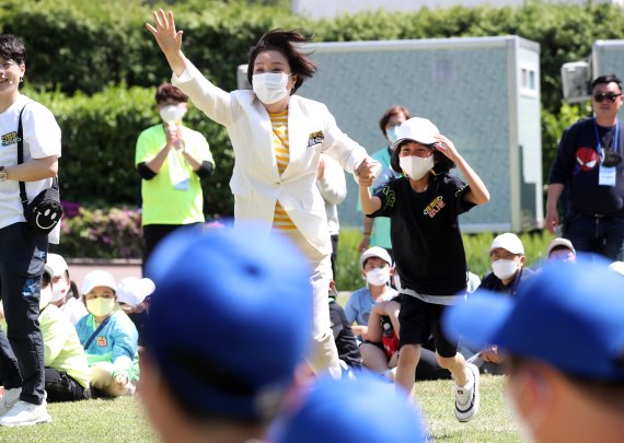 [서울=뉴시스] 전신 기자 = 문재인 대통령 부인 김정숙 여사가 5일 청와대 녹지원에서 열린 2022년 어린이날 100주년 기념 청와대 어린이 초청행사에서 머리 위로 큰공 굴리기 첫번째 경기에서 승리한 후 한 아이의 손을 잡고 사회자에게로 달려가고 있다. 2022.05.05. photo1006@newsis.com