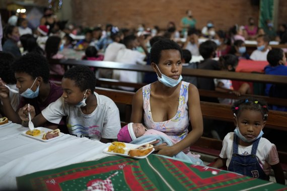 [카라카스=AP/뉴시스] 21일(현지시간) 베네수엘라 카라카스의 산 미겔 아크엔젤 교회 무료 급식소에 한 여성이 갓난 아이를 안고 딸과 함께 앉아 있다. 이 무료 급식소는 크리스마스를 맞아 젖먹이 엄마를 포함한 약 200명의 아이들에게 베네수엘라 전통 식사를 제공했다. 2021.12.22.