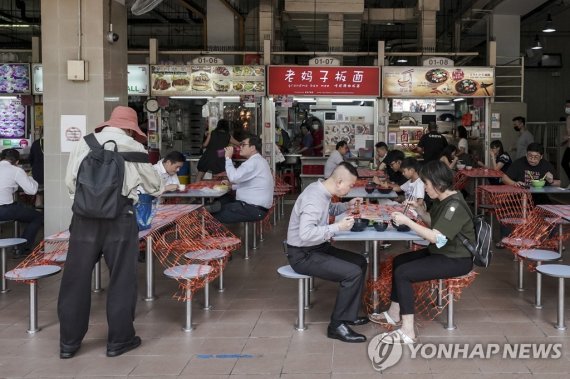 싱가포르 호커센터 epa09290013 Patrons sitting in pairs at cordoned off tables at the Amoy Street Food Centre in Singapore, 21 June 2021. Singapore has lifted its Phase 2 (Heightened Alert) COVID-19 restrictions on dining-in at restaurants, eateries, and hawker centres but capped the number of patrons dining