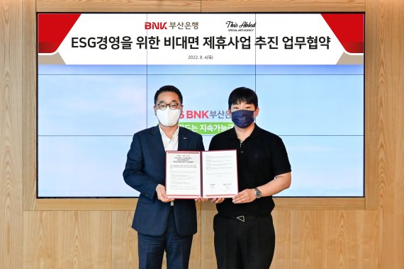 BNK부산은행 김양욱 언택트영업부장(왼쪽)과 디스에이블드 김현일 대표가 업무협약서를 들고 기념사진을 찍고 있다./제공=부산은행