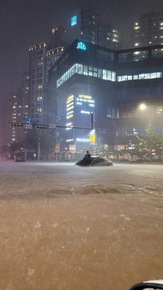 온라인 커뮤니티에서 화제가 된 '강남역 제네시스'. 서울과 경기북부 등 수도권에 폭우가 내린 지난 8일 저녁 서울 강남역 인근 한 제네시스 차주가 차 위에 올라가 비가 멎기를 기다리고 있다.