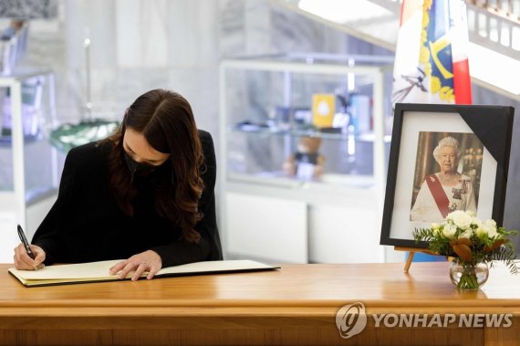 여왕 사진 곁에서 추모 메시지 작성하는 뉴질랜드 총리 New Zealand's Prime Minister Jacinda Ardern writes in a condolence book for Britain's Queen Elizabeth II at Parliament in Wellington on September 9, 2022. - Queen Elizabeth II, the longest-serving monarch in British history and an icon instantly recognisable to billions