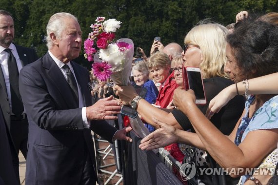 꽃다발 건네받는 찰스 3세 Britain's King Charles III, left, greets well-wishers as he walks by the gates of Buckingham Palace following Thursday's death of Queen Elizabeth II, in London, Friday, Sept. 9, 2022. King Charles III, who spent much of his 73 years preparing for the role, planned to meet with the pri