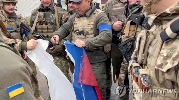 12일(현지시간) 우크라이나 하르키우지역을 다시 탈환한 우크라이나 군인들이 러시아 국기를 찢고 있다. 비디오 영상 캡쳐. /로이터 연합뉴스