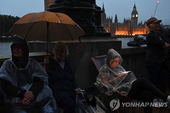 여왕의 관을 직접보기 위해 웨스트민스터 홀 강건너까지 늘어선 조문객들 TOPSHOT - Members of the public queue in the rain along the south bank of the River Thames, opposite the Palace of Westminster, home to Westminster Hall and the Houses of Parliament, in London on September 13, 2022, as they wait to pay their respects when Queen