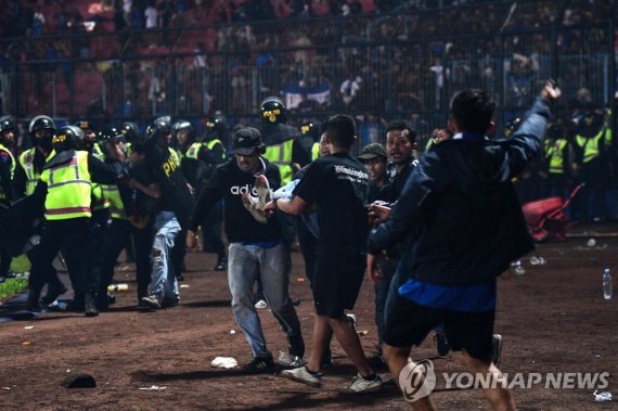 In this picture taken on October 1, 2022, a group of people carry a man at Kanjuruhan stadium in Malang, East Java. - At least 127 people died at a football stadium in Indonesia late on October 1 when fans invaded the pitch and police responded with tear gas, triggering a stampede, officials said. (