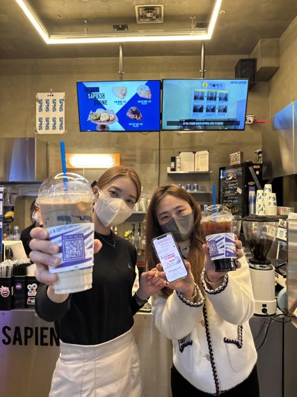 9일 미디어로그 모델들이 커피사피엔스 상암점에서 브랜드콜라보가 진행 중인 컵 홀더의 QR코드를 스캔해 이벤트에 응모하고 있다. 미디어로그 제공