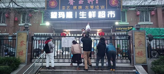 25일 오후 중국 베이징 차오양구 왕장의 한 아파트 내부 대형 마트 직원이 철 담벼락 사이로 생필품을 건네주고 있다. 사진=정지우 특파원