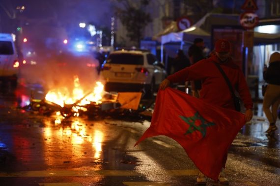 27일(현지시각) 벨기에 브뤼셀의 한 거리에서 2022 카타르 월드컵 모로코와 벨기에전이 끝난 뒤 폭동이 일어났다. 모로코 국기를 든 한 남성이 불타는 거리를 걸어가고 있다. 출처 EPA 연합뉴스