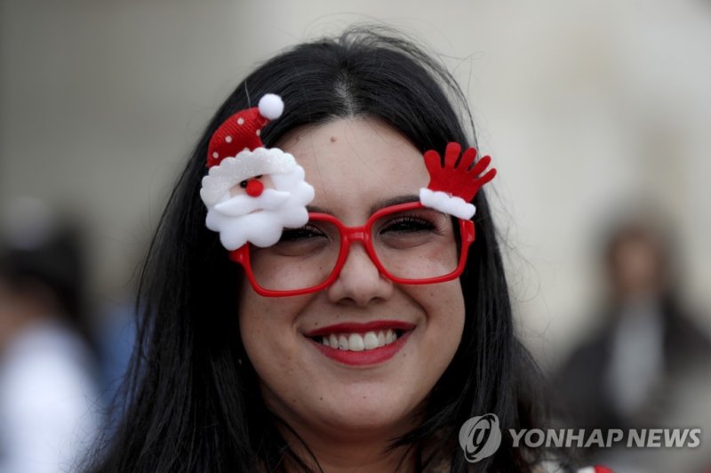 예수 탄생 교회 앞에서 산타글로스 장식의 안경을 쓰고 웃는 관광객. epa10377693 A tourist wearing a Santa glasses looks on during Christmas Eve procession at Manger Square, leading to the Church of the Nativity, in the West bank town of Bethlehem, 24 December 2022. The Church of the Nativity is one of the oldest continuously ope