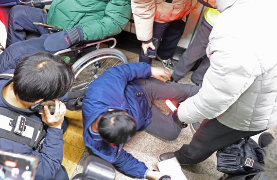 삼각지역장(가운데)이 3일 서울 삼각지역에서 전국장애인차별철폐연대에 안내 방송을 하던 도중 휠체어에 치여 쓰러지고 있다.전장연은 올해 주말과 공휴일을 제외하고 매일 출근길 지하철 시위를 하겠다고 밝혔다. 사진=김범석 기자