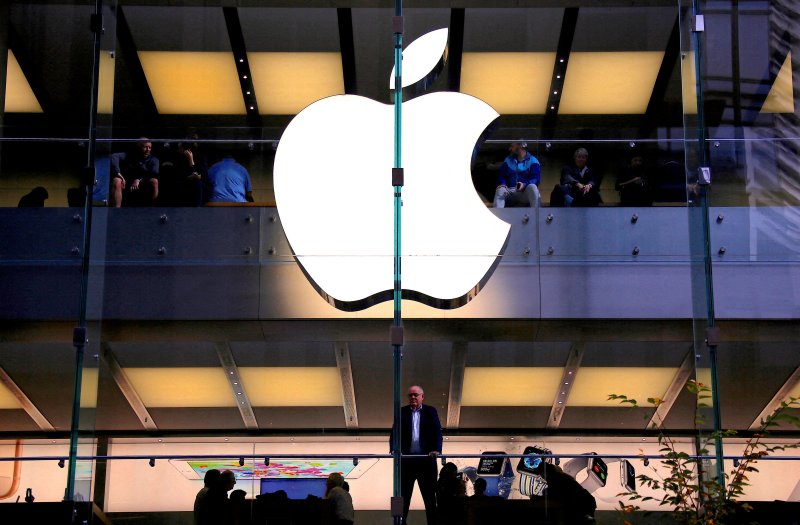 FILE PHOTO: FILE PHOTO: A customer stands underneath an illuminated Apple logo as he looks out the window of the Apple store located in central Sydney, Australia, May 28, 2018. REUTERS/David Gray/File Photo/File Photo