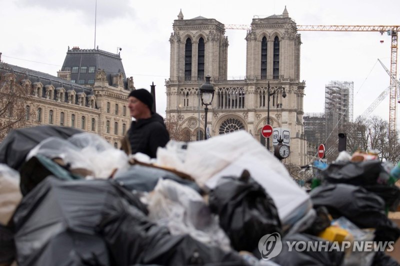 쓰레기로 뒤덮인 파리 A pedestrian walks past garbage bags that have been piling up in front of Notre Dame de Paris as waste collectors are on strike since March 6 to protest against the French government's proposed pensions reform, in Paris on March 22, 2023. (Photo by ALAIN JOCARD / AFP)