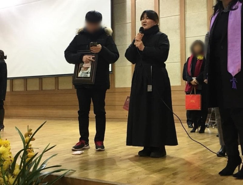 학폭 피해자 고(故) 박주원양의 어머니 이기철씨가 2018년 은광여고 졸업식에 딸의 영정사진을 들고 참석해 단상에서 발언하고 있다. (이기철씨 페이스북)