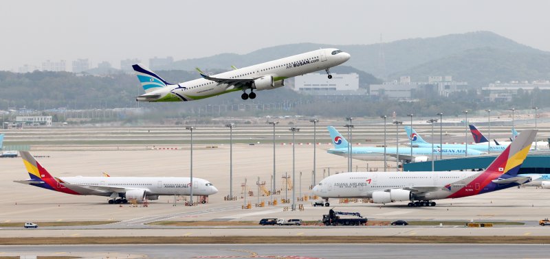 지난달 24일 오후 인천국제공항 주기장에 세워진 대한항공, 아시아나항공 여객기 위로 에어부산 여객기가 이륙하고 있다. 연합뉴스