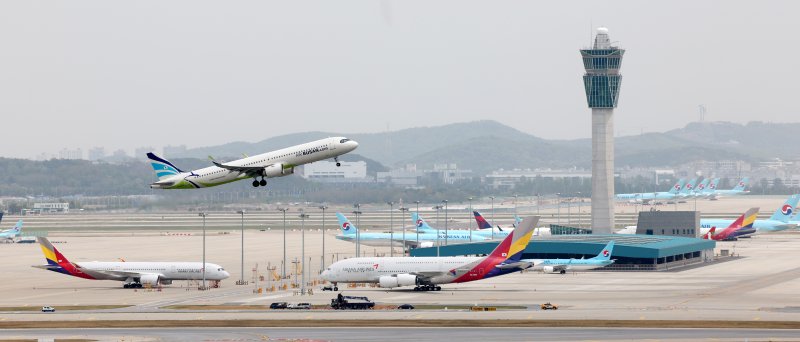 지난 4월 24일 오후 인천국제공항 주기장에 세워진 대한항공, 아시아나항공 여객기 위로 에어부산 여객기가 이륙하고 있다. 연합뉴스 제공