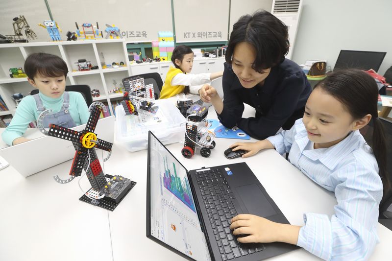 선생님이 어린 학생들에게 KT AI 코디니를 이용해 코딩과 하드웨어 융합 교육을 진행하고 있다.