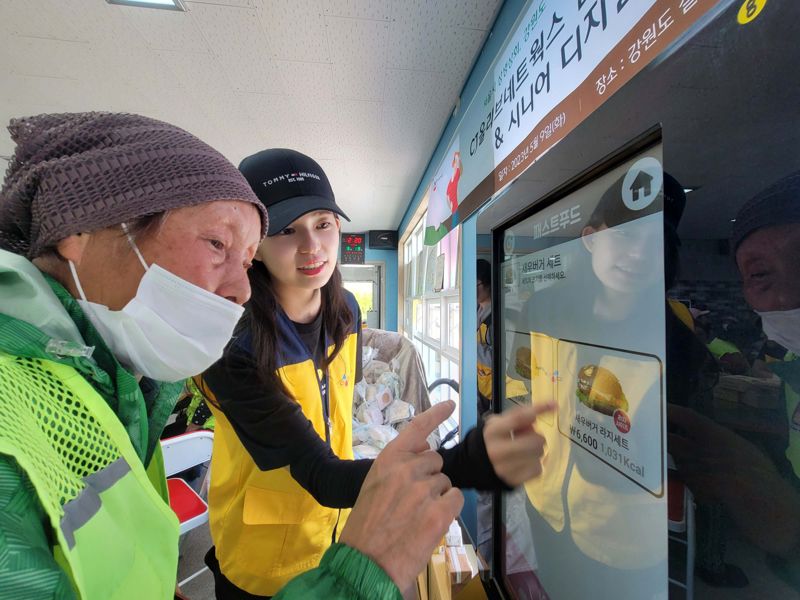 CJ올리브네트웍스 임직원이 지난 9일 강원도 철원군 패스트푸드점에서 어르신께 키오스크 사용법을 알려주고 있다. CJ올리브네트웍스 제공