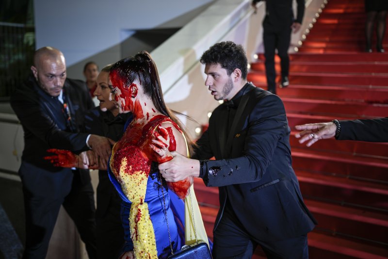 [칸=AP/뉴시스] 우크라이나 국기 색상 옷을 입은 여성이 21일(현지시각) 프랑스 남부 칸에서 열린 제76회 칸 국제영화제 '애시드' 시사회장에 난입해 붉은색 액체를 몸에 붓던 중 보안요원들에게 붙잡혀 끌려 나가고 있다. 2023.05.22.