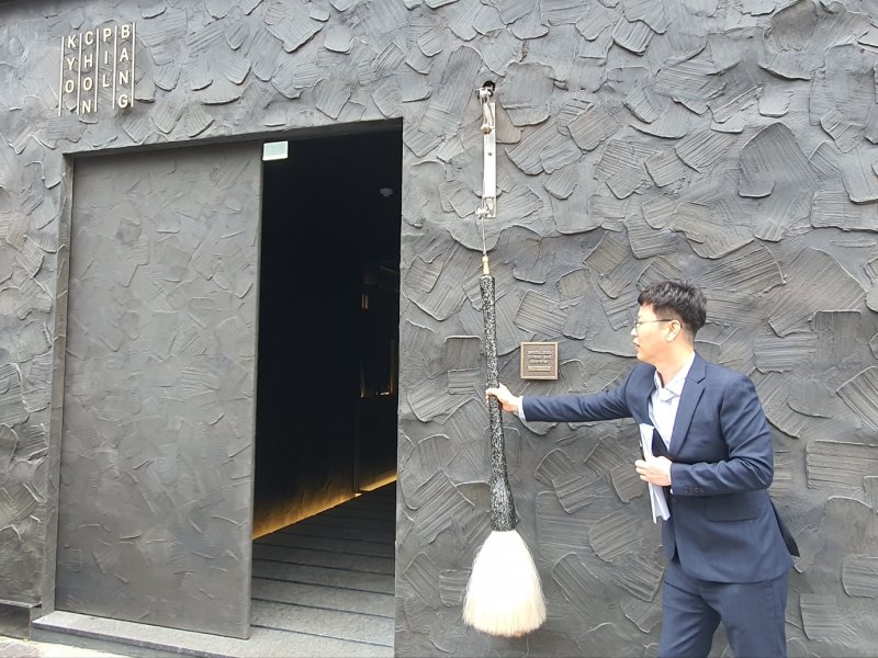 [서울=뉴시스]김혜경 기자 = 교촌에프앤비 관계자가 7일 서울시 용산구 이태원동에 위치한 '교촌필방' 출입구에서 '붓'을 잡아 당겨 문을 여는 모습을 시연하고 있다. 2023.06.07.