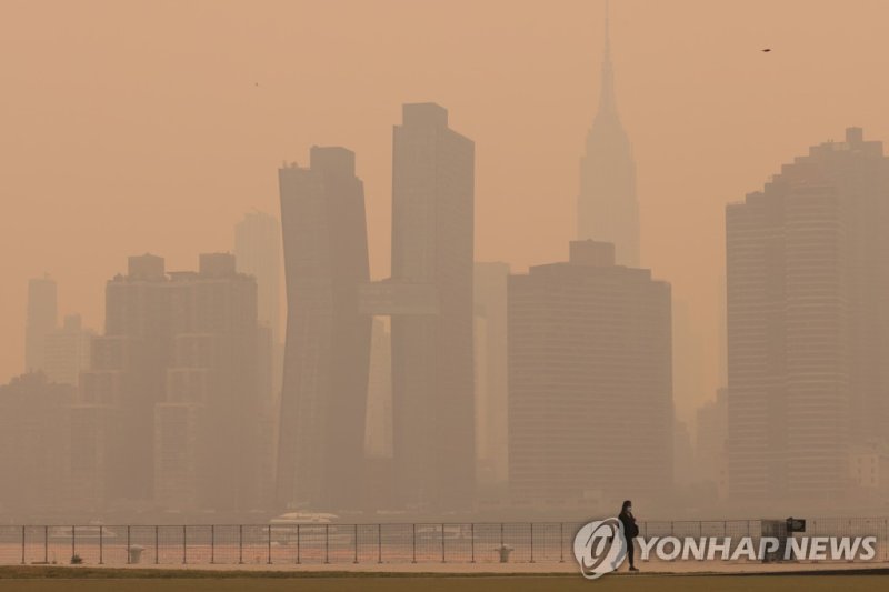 연기로 뒤덮인 뉴욕 시내 전경 A woman walks along the East River in Long Island as haze and smoke caused by wildfires in Canada hang over the Manhattan skyline, in New York City, New York, U.S., June 7, 2023. REUTERS/Andrew Kelly