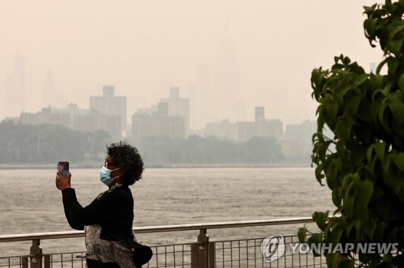 연기로 뿌옇게 뒤덮인 뉴욕 맨해튼 일대 A person wearing a face mask takes a picture of the Manhattan skyline while it's covered in haze and smoke caused by wildfires in Canada, in Brooklyn, New York, United States, June 7, 2023. REUTERS/Amr Alfiky