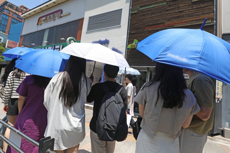 대구와 경북 일부 지역에 올여름 첫 폭염주의보가 발효된 17일 대구 중구 동성로의 한 아이스크림 판매점 앞에 아이스크림을 사려는 시민들이 매장에서 임시로 제공한 양산과 우산으로 뙤약볕을 가리며 차례를 기다리고 있다. 2023.6.17/뉴스1 ⓒ News1 공정식 기자